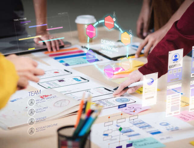 Foto. Auf einem Tisch liegen Planungsnotizen. Verschiedene Hände interagieren mit den Notizen. Das analoge Geschehen wird erweitert durch die Ansicht digitaler Anwendungen zur Planung von Gruppenarbeit. Bildschirmfotos dieser Anwendungen erscheinen über dem Tisch.